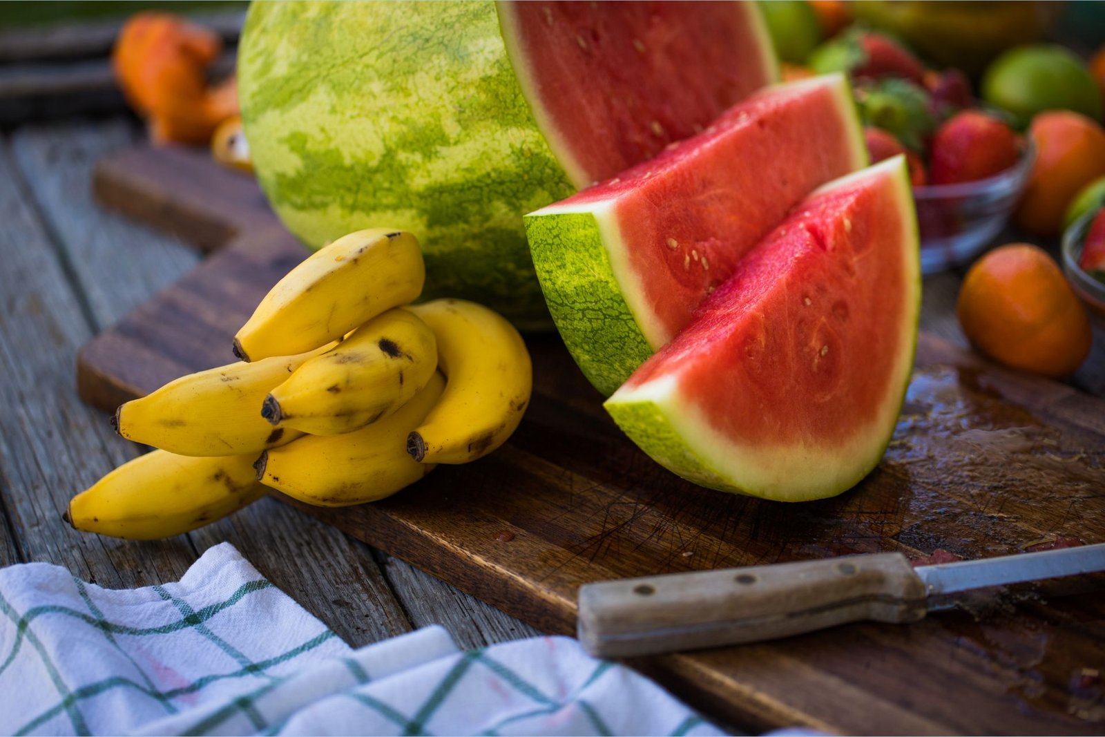 Banane, bogate s kalijem, ležijo na deski za rezanje poleg narezane lubenice, bogate z L-citrulinom.