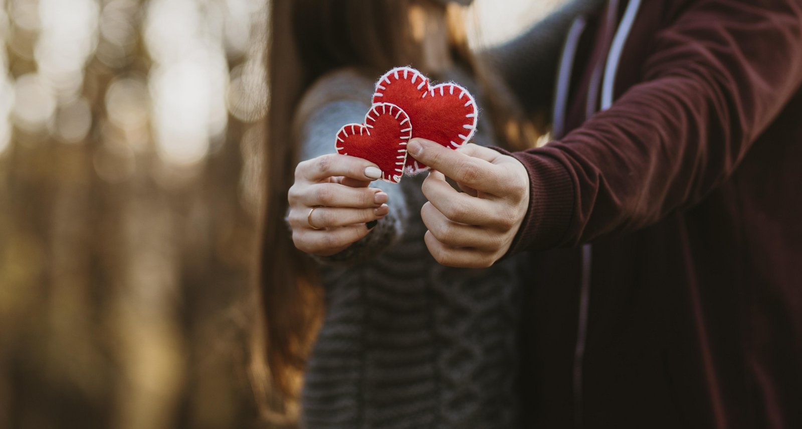 Zaljubljenca za valentinovo držita v rokah dve rdeči srčki